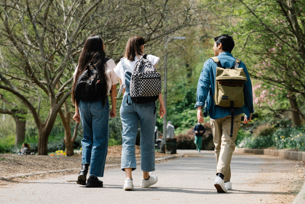 Three students walk on a walking path surrounded by trees.