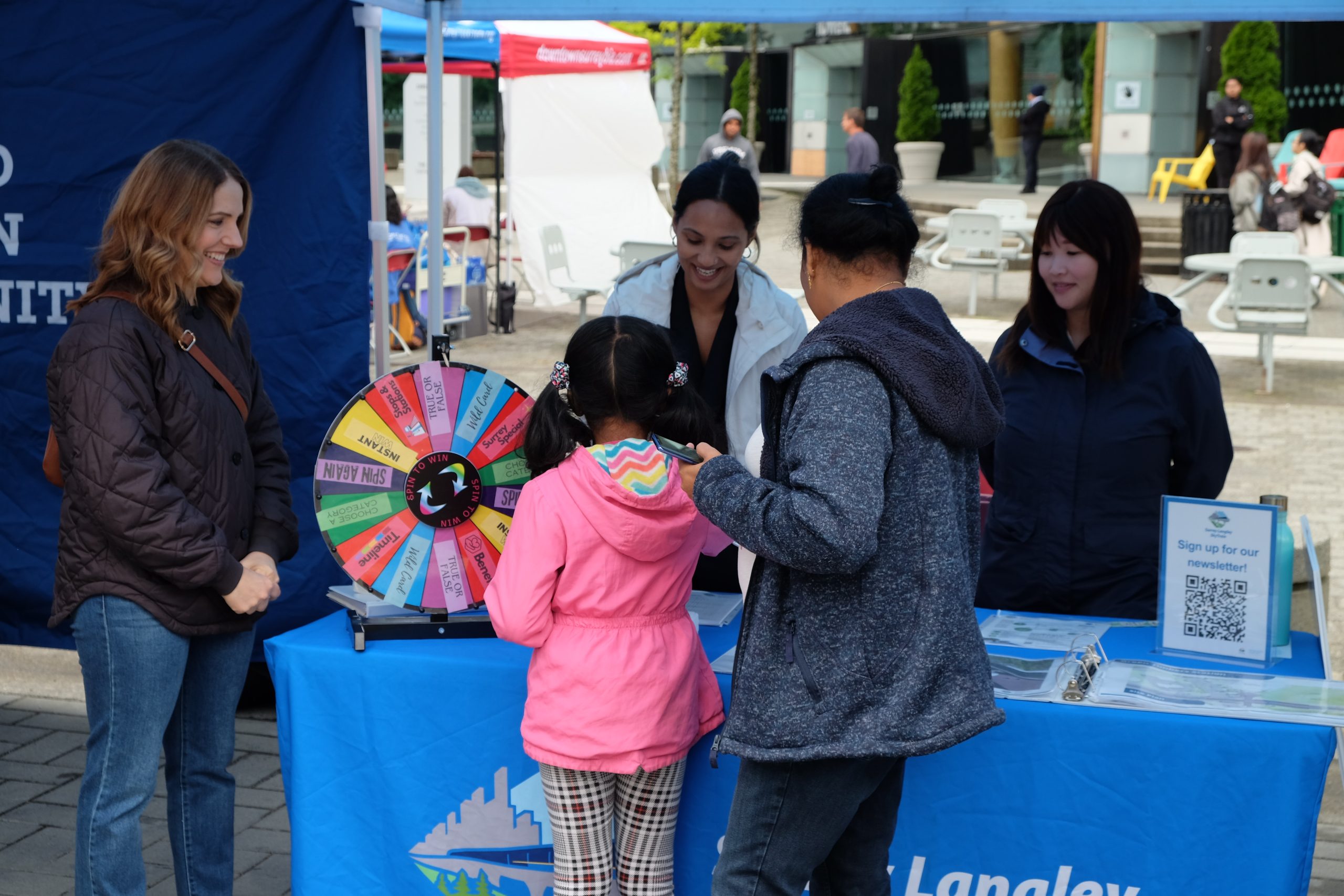 Surrey Langley Skytrain team members engage with a local family at an outdoor booth during the Surrey Fest in Surrey, BC.