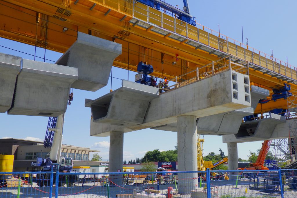 An image showing a specialized lifting machine, known as a launching gantry, lifting elevated guideway segments into place to build the Surrey Langley SkyTrain elevated guideway.